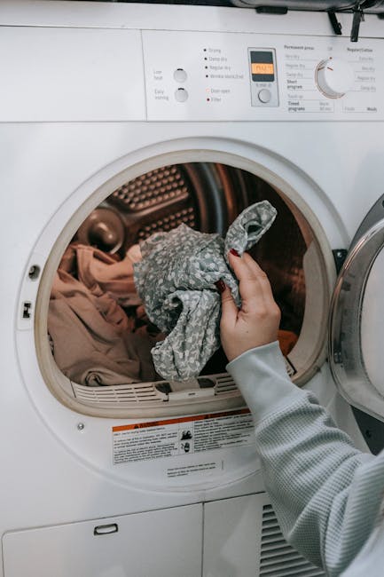 Crop unrecognizable female loading dirty clothes in modern white washing machine while doing housework routine in light room at home